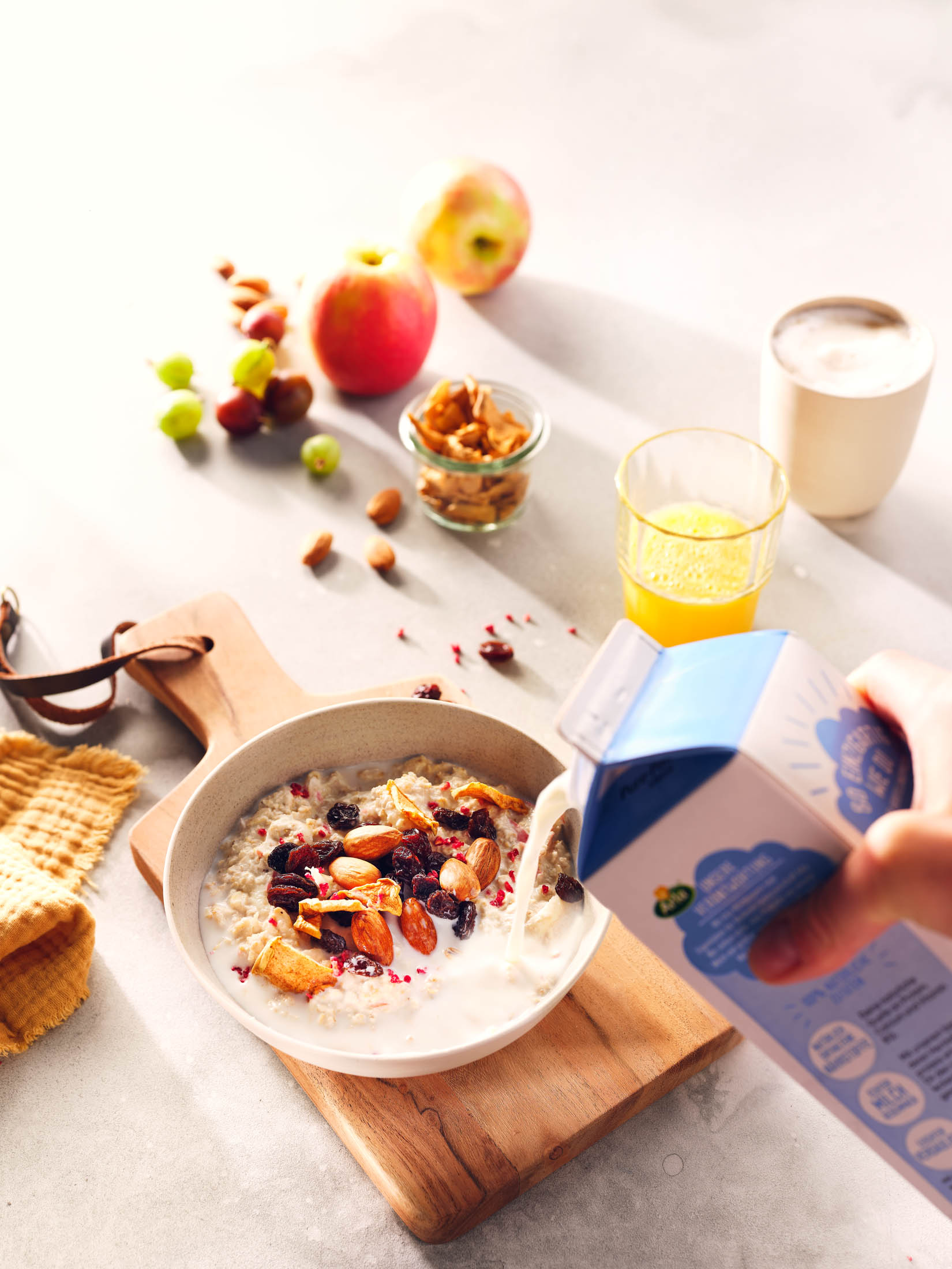 Rezeptbild für femtastics und arla - Birchermüsli auf einem Frühstückstisch in warmen gleißenden Licht, auf das gerade Milch gegossen wird - Fotografie von Studio hackenberg in Hamburg