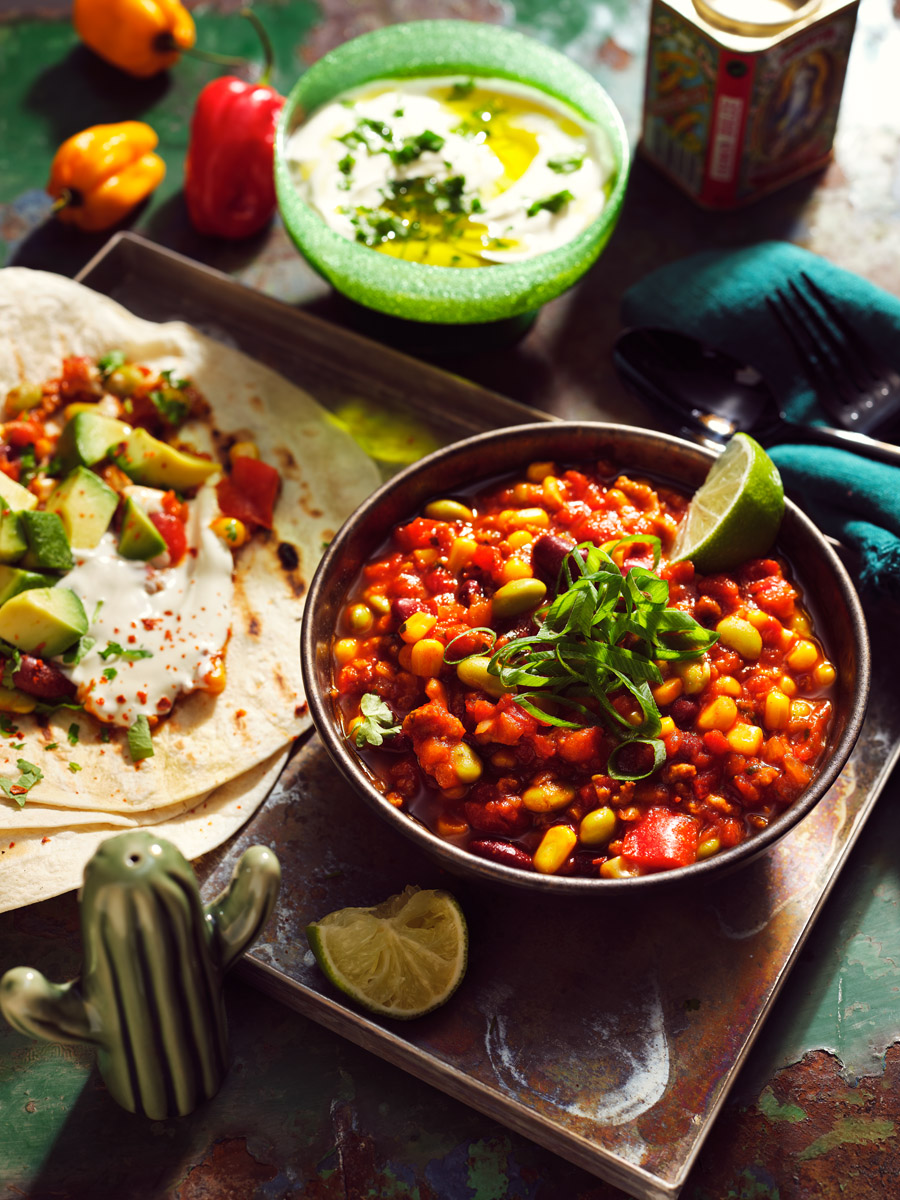 Lebendige Aufnahme von Tacos und Chili Sin Carne, welches gerade auf einem Tisch zubereitet wird. Foodofografie vom Studio hackenberg